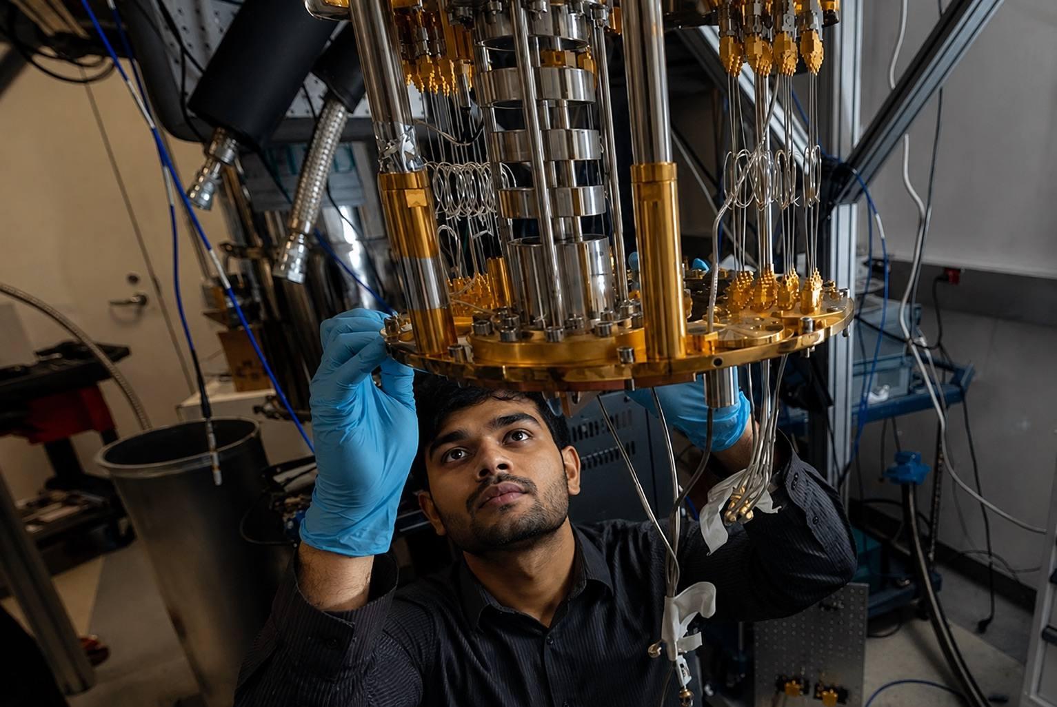 An engineer in lab gloves adjusting the gold-plated wiring stages of a dilution refrigerator.